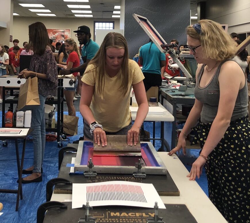Student screen printing a poster in the library's lobby.