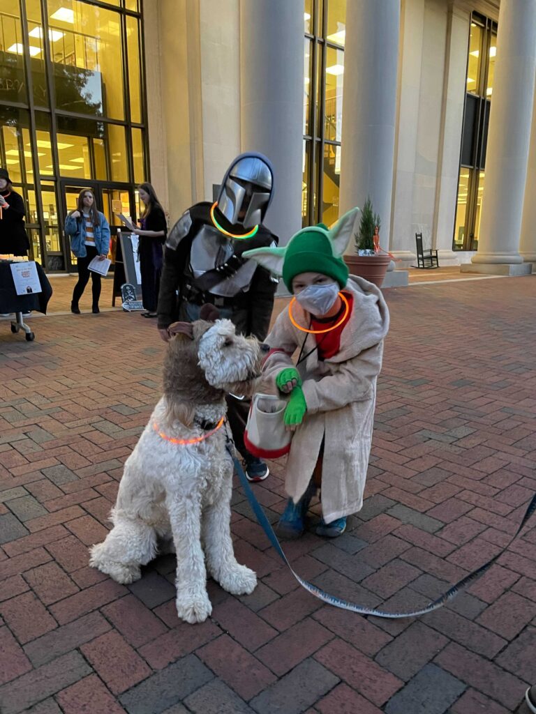 Kids dressed like Yoda and the Mandalorian with a dog dressed like an Ewok- standing in front of the library