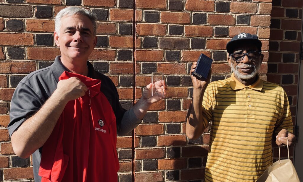 Dave Heinz and Michael Forney standing against brick wall holding awards.