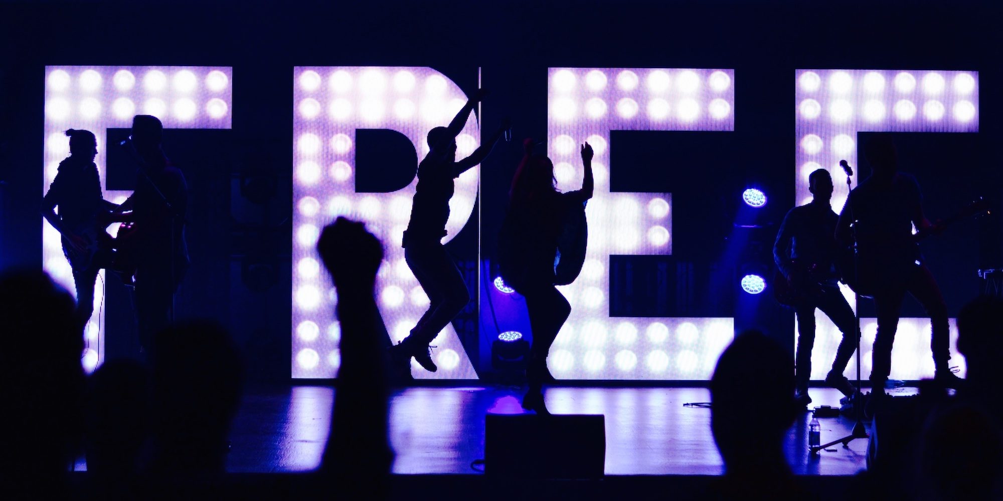 people dancing on concert stage in front of the a light display that reads "free"