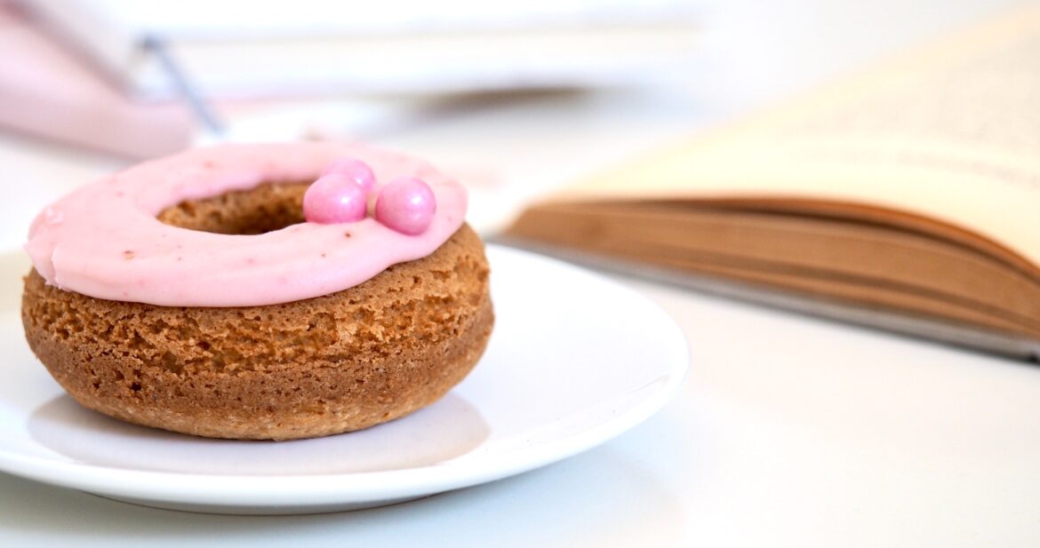 Pink donut on table next to a book