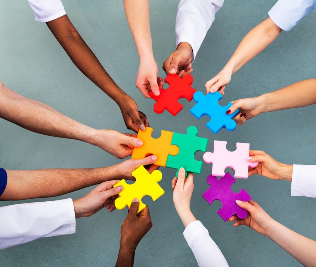 Many hands holding pieces to a puzzle in the center.