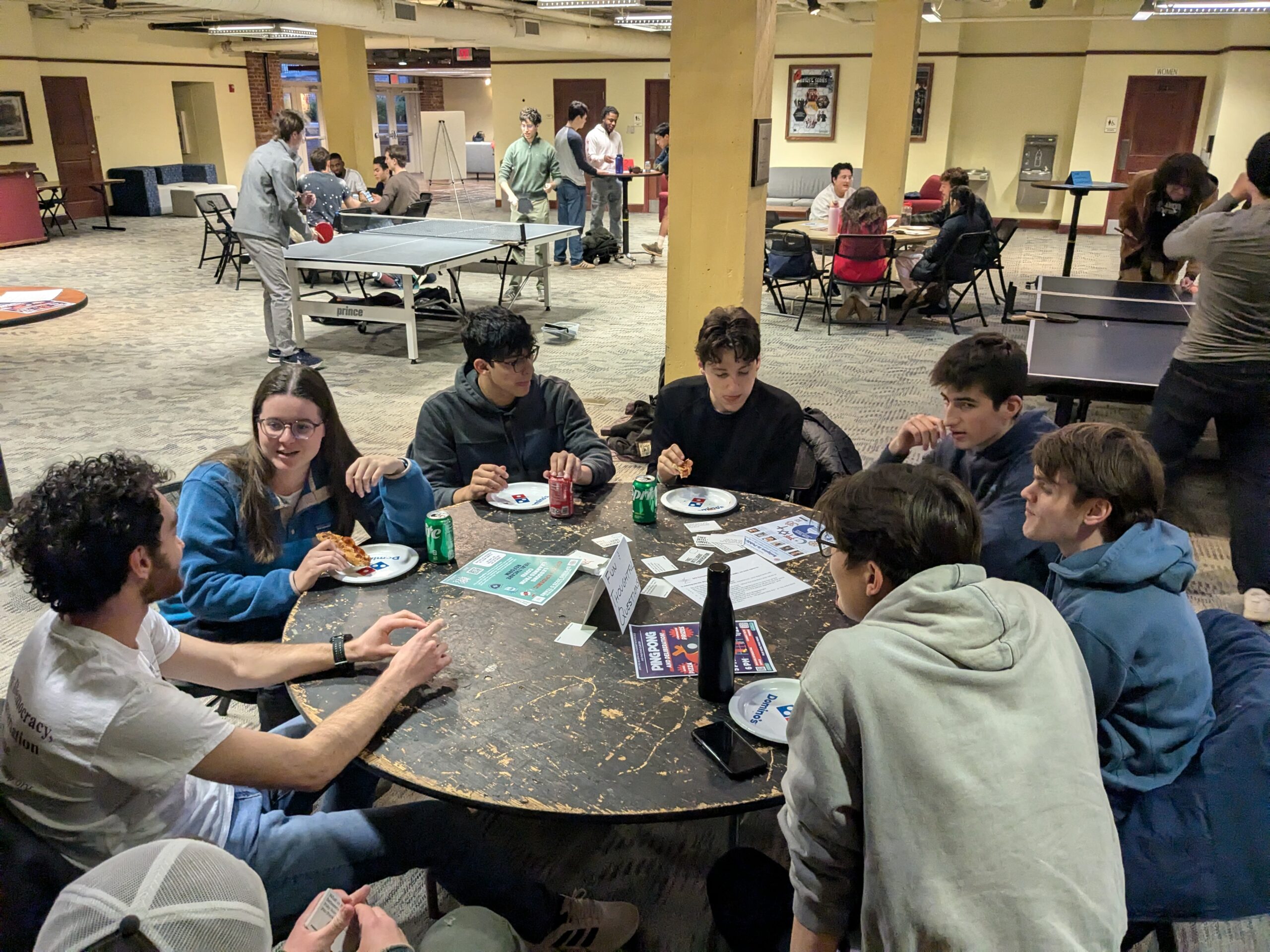photo of students deliberating around a table with ping pong in the background.