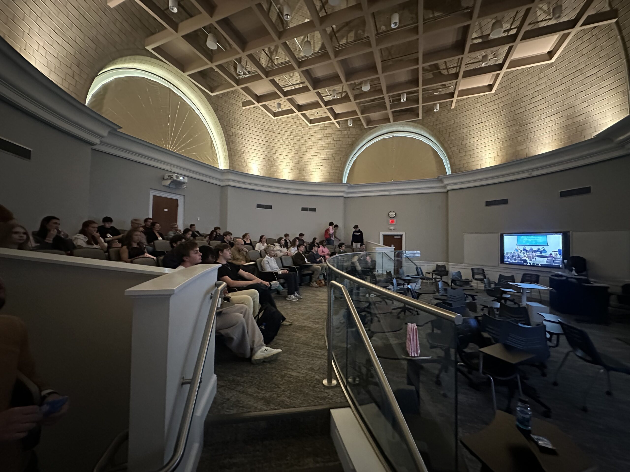 Photo of auditorium with audience and tv showing expert roundtable.