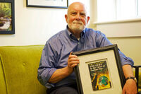 Dr. Randy Nelson in his office, holding a framed copy of Tom Swift in the Caves of Nuclear Fire