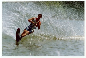 A man Water sking and leaning to his left making a splash wave