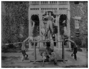 A photo that was torn in half and put back together of gymnasts doing handstands and balancing on one another in front of a building covered in ivy