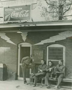 4 men sitting on a bench outside of the "Student Store" featuring a Coca Cola sign