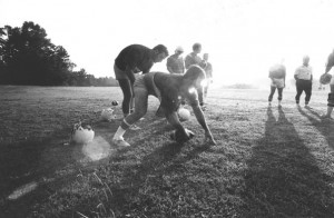 Wildcat football practice August 25, 1980, a center snapping to the quarterback with the sun setting/glistening in the background