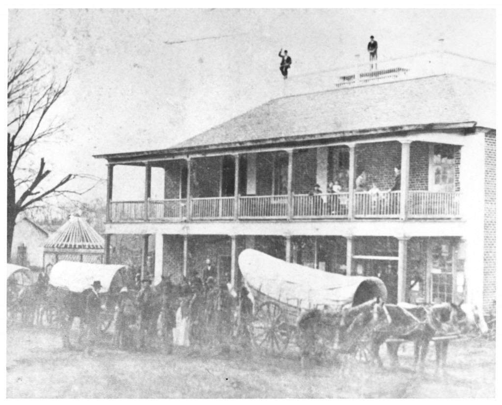 Carolina Inn as the Helper Hotel, circa 1870s., two people standing on the roof with two carriages out front and many people standing outside