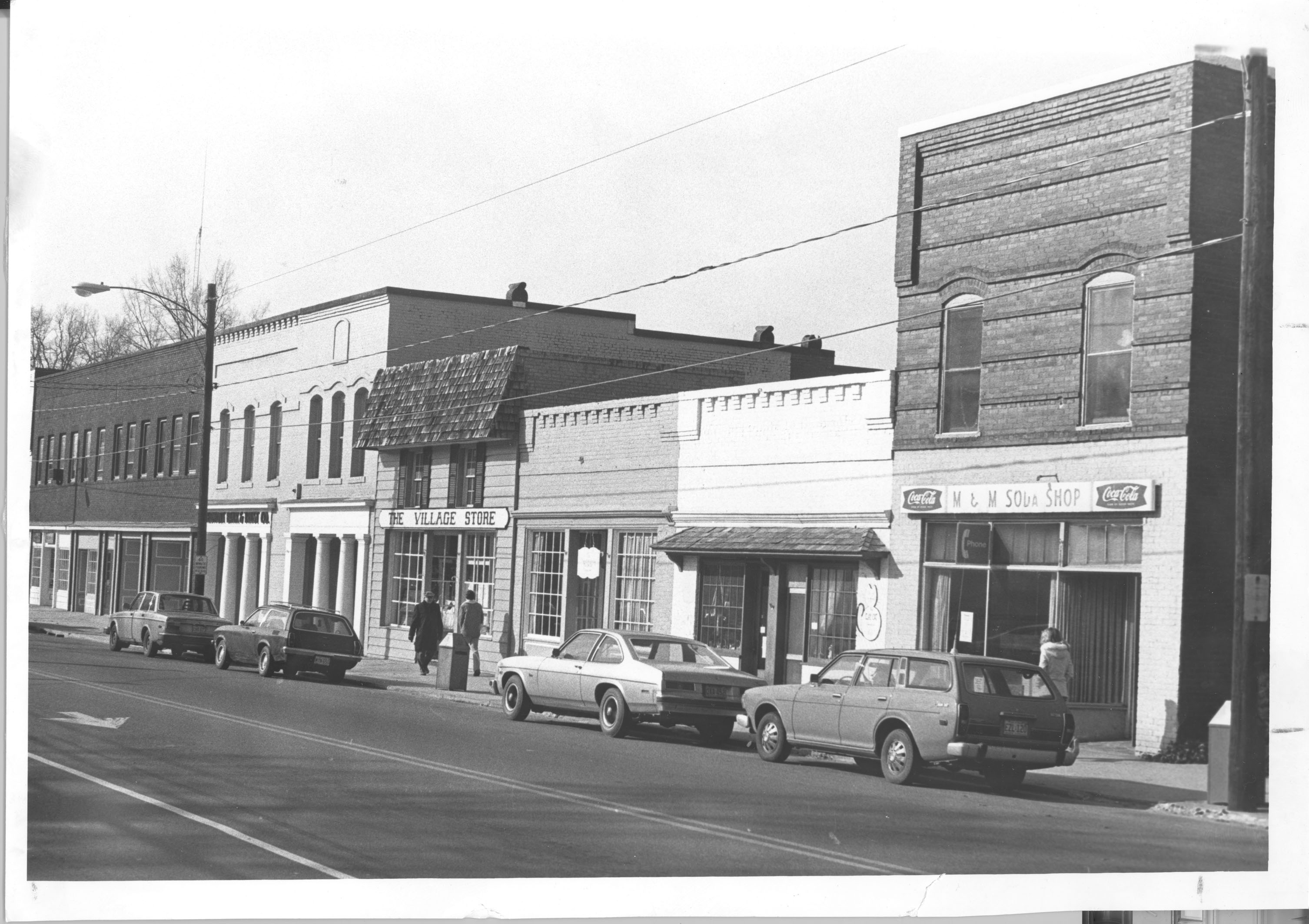 Photograph of the Davidson Historic District, now found in the Wikimedia Commons Summer of Monuments project. It is a picture of main street with 4 cars parked on the side of the road, The stores include M & M Soda Shop, The Village Store and a few others without signs