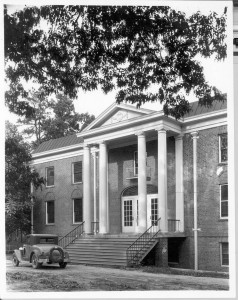 Alumni Gymnasium entrance, has four pillars and steps leading up to the front (four) doors. There is a car at the bottom of the steps