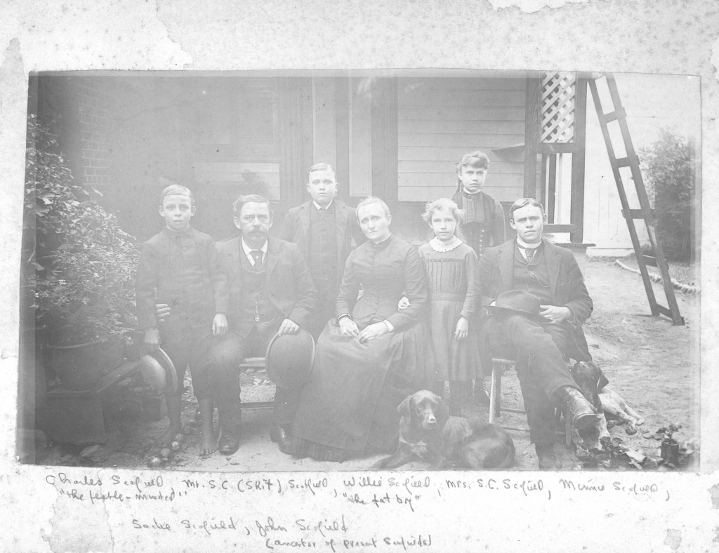 The Scofield family in front of their home. There dog is also laying in the front.