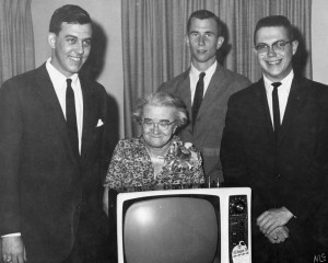 Miss Johnsie Shelton with Pi Kappa Phi brothers standing in front of a tv