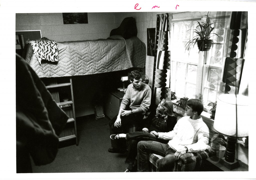 Three students gather in a mid-1980s dorm room - note the lofted bed, now a very popular dorm room modification.