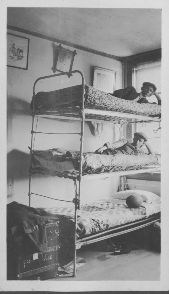 Triple decker bunk bed, the top and middle bunk has a person on it, the lowest bunk has a football on it, three picture frames on the wall with a trunk at the foot of the bed