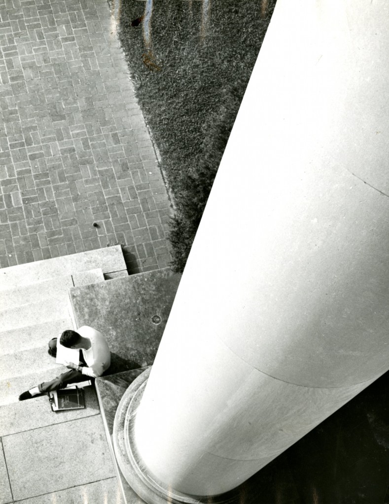 An ariel view of an unknown student reads at the base of a pillar in front of Chambers Building.