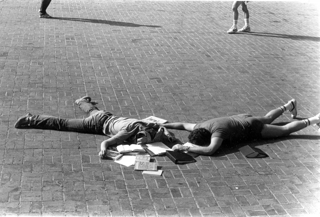 Two students laying on the brick path with books scattered around them outdoors, circa 1994.