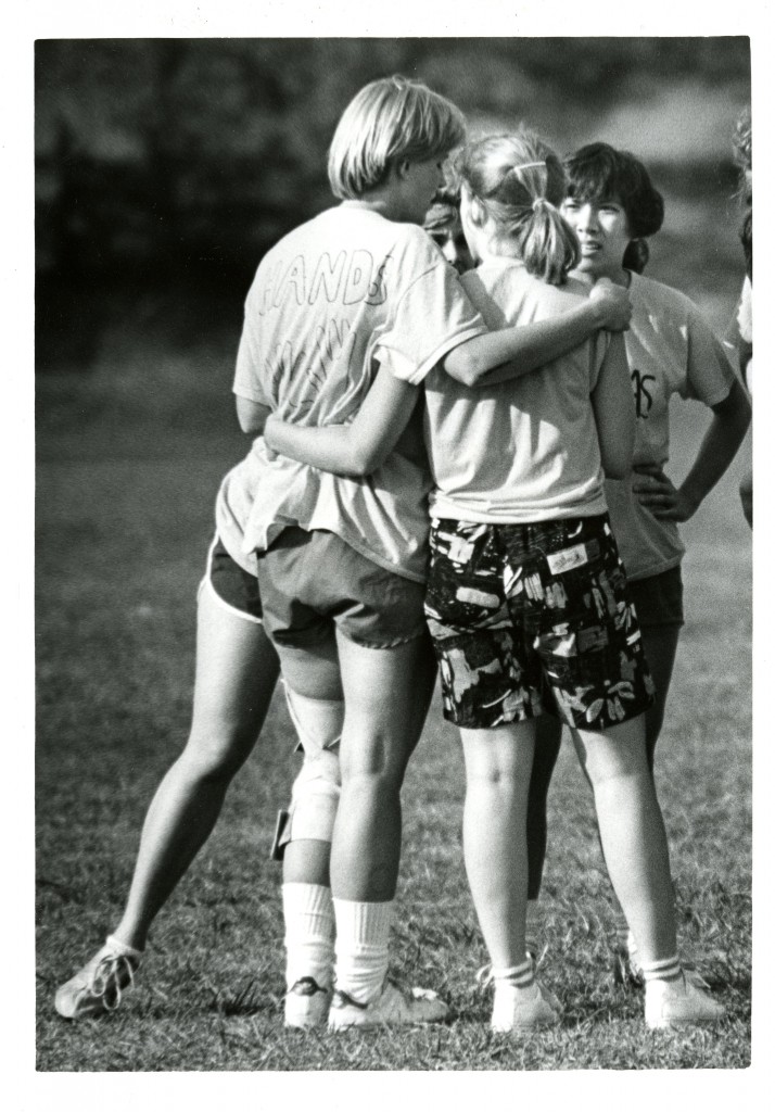 The caption on the back of this photograph reads: Flickerball - Fall '85 - Rusk - Lillean Woo - '86." The image is of players huddling, who are on the 1985 Rusk House flickerball team, including Lillian Grace "Beadsie" Woo (Class of 1986).