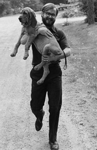 A man carrying a dog down a gravel road