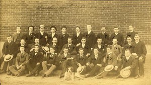 From the John Hunter Grey photograph collection. A photo of 28 men with suits, some having hats and canes, with a dog in the front