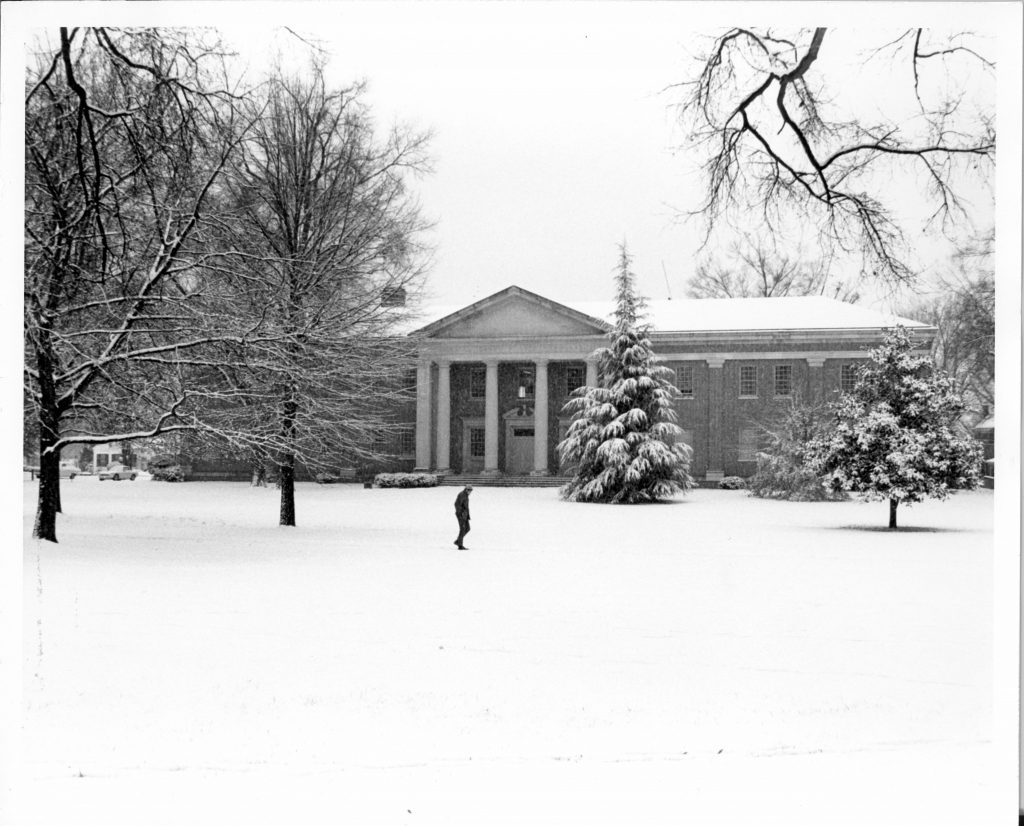 A lone figure walks past Dana Science Building in the snow, 1969.