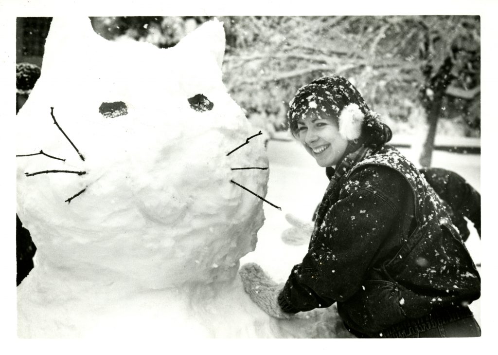 A student looking over her left shoulder toward the camera leaning on a large snow cat she just made.