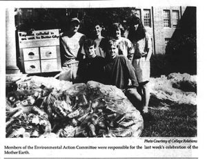 1990 Earth Day trash display, students standing next to large plastic bags filled with trash, one of them holding a sign