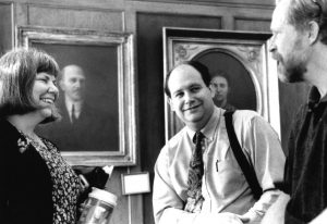 Past AAG Officers, Marcia Makl, Kurt C. Holmes, William Brown standing before a portrait gallery ca. 1996-2001