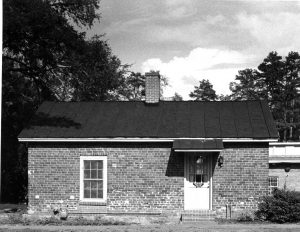 Small brick building with a covered doorway, one window and a chimney. 