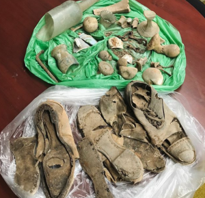 A green plastic bag with broken animal bones and glass pieces. A clear plastic bag with old, worn pairs of shoes. 