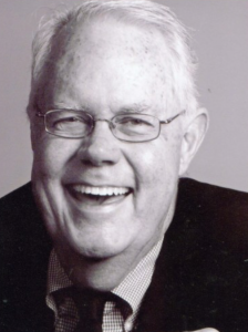 Headshot of a laughing man wearing glasses, black and white.