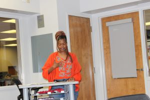 Woman stands at podium in orange shirt.