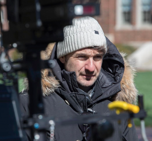 A man in a parka and winter hat stands behind film cameras. 