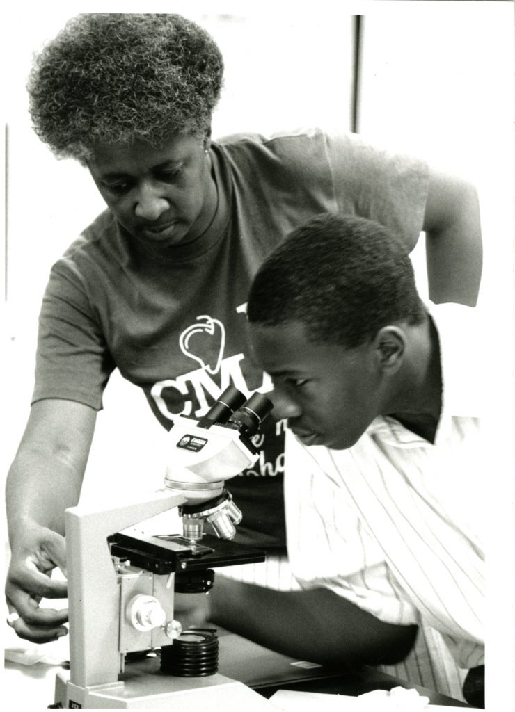 A black professor assists a black student with a microscope as part of the 1995 Love of Learning summer program.