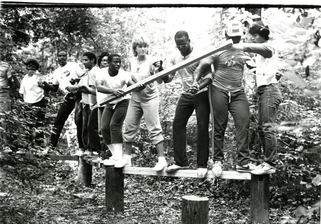 A group of about one dozen students balancing on a log as part of the August 1984 FOCUS Davidson College orientation program.