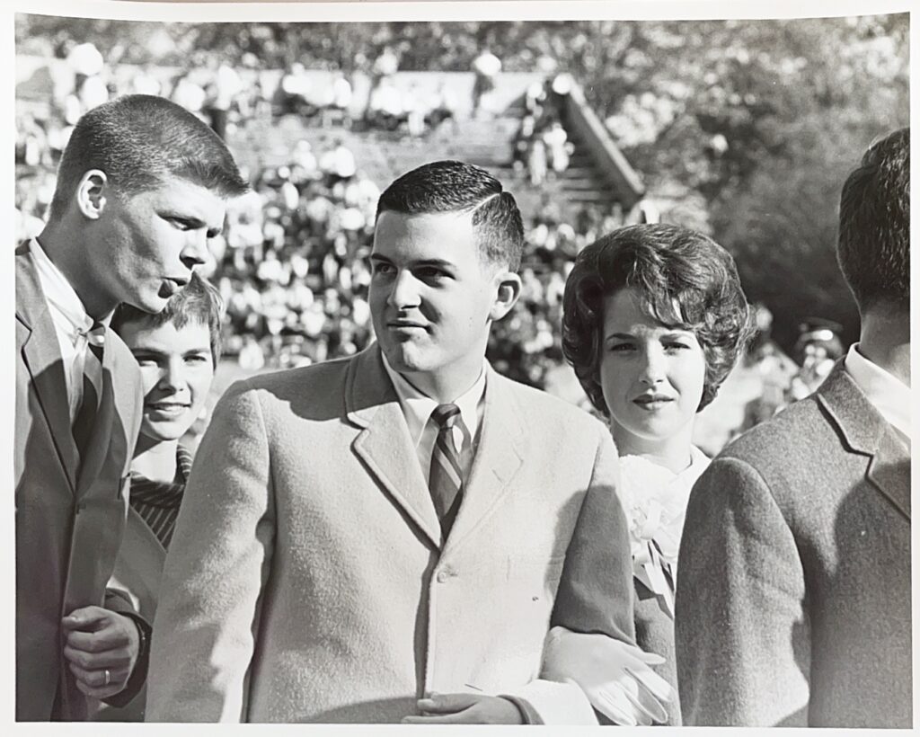 Dates line up in formal attire in front of a football stadium. 