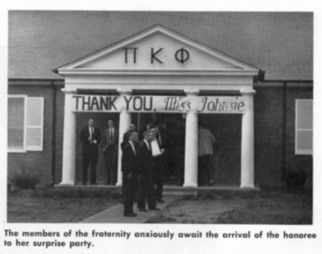 Several men stand in front of the Pi Kappa Phi fraternity house. The front of the house has a banner across that reads, "Thank you, Miss Johnsie."